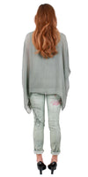 Woman in sage green silk top and printed linen pants, back view, wearing black heels