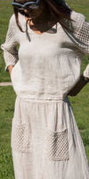 Woman outdoors wearing a beige linen dress with crochet sleeves and front pockets
