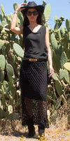 Woman in a sleeveless black silk top, mesh skirt, and hat posing outdoors by cacti