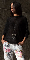 Woman in a sparkly black top, floral white pants, and heart pendant necklace outdoors