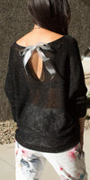 Woman wearing a sheer black knit top with silver ribbon back tie and floral print pants