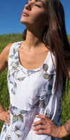 Woman in sleeveless white floral linen dress standing in sunny green field