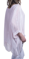 Woman wearing a loose light pink silk blouse with draped sleeves and white pants