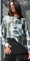 Woman in an artistic face print sweater and black skirt, standing by a chain-link fence