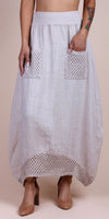 Woman wearing a light linen maxi skirt with crochet pockets and hem, paired with block heels.