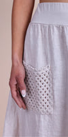 Close-up of a beige linen skirt with a crochet pocket detail, worn by a woman