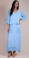 Woman wearing a light blue linen maxi dress with crochet sleeves, pockets, and hem