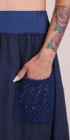 Woman with floral tattoo placing hand in navy crochet pocket on linen skirt