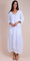 Woman wearing a white linen dress with crochet sleeves, pockets, and hem, standing indoors