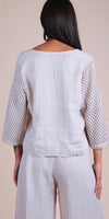 Back view of woman wearing white linen top with crochet sleeves and matching linen pants
