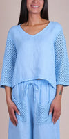 Woman wearing light blue linen top with crochet sleeves and matching pants with crochet pockets