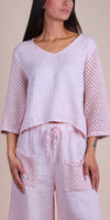 Woman wearing light pink linen two-piece set with crochet sleeves and pockets, v-neck top.