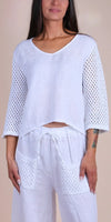 Woman wearing white linen top with crochet sleeves and drawstring pants with crochet pockets