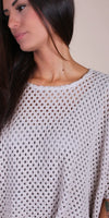 Woman wearing a loose-knit white crochet top with wide sleeves, close-up view