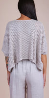 Back view of woman in light grey crochet knit top and loose linen pants