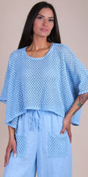 Woman wearing light blue crochet knit top with wide sleeves and matching linen pants with pockets