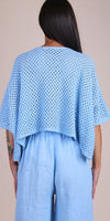 Woman wearing light blue crochet knit top and loose linen pants, back view