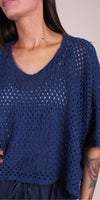 Woman wearing a loose-knit navy blue crochet top with short sleeves and scoop neckline