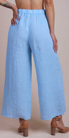 Back view of woman wearing light blue wide-leg linen pants and brown heel sandals