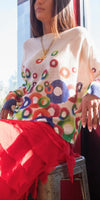 Woman wearing a colorful circle-pattern knit sweater and red ruffled skirt by a window
