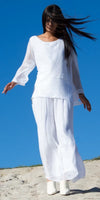 Woman in airy white linen outfit and boots standing outdoors under clear blue sky