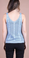 Back view of woman wearing light blue knit sleeveless top with cable detail and black pants