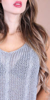 Woman wearing light grey cable knit sleeveless top with wavy brown hair