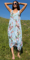 Woman in blue floral linen dress and sunglasses standing barefoot in grassy field