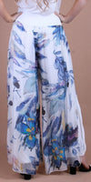 White wide-leg floral print silk pants with blue and yellow flowers, modeled from behind.