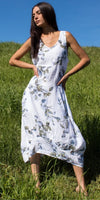 Woman in sleeveless floral linen dress standing in grassy field under blue sky