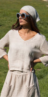 Woman in beige linen dress with crochet sleeves and pockets, wearing sunglasses and headscarf outdoors