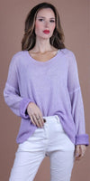 Woman in light purple knit sweater and white pants against a neutral background