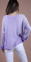 Woman wearing lavender knit sweater and white pants, seen from the back