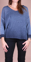 Woman wearing loose knit blue sweater with black pants, neutral background