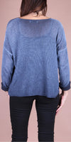 Back view of woman wearing loose blue knit sweater and black pants on neutral background