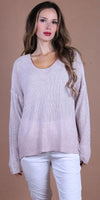 Woman wearing a loose-knit light pink sweater and white pants, neutral brown background