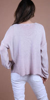 Back view of woman in light pink knit sweater and white pants on neutral background