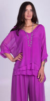 Woman wearing loose fit, layered purple silk top and matching wide-leg pants, accessorized with a long beaded necklace