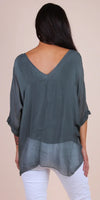 Back view of woman wearing loose sheer gray V-neck blouse and white pants