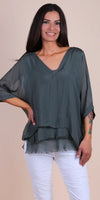 Woman wearing a loose-fit dark gray silk blouse with v-neck and white pants