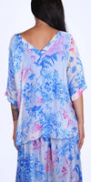 Back view of woman in blue and pink floral silk blouse and skirt, V-neck design