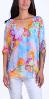 Woman wearing a colorful abstract print blouse with V-neck and white pants