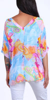 Woman wearing loose-fit V-back pastel blouse with abstract swirl print and white pants