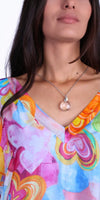 Woman wearing a colorful heart print V-neck top with a round pendant necklace