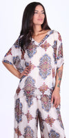 Woman wearing flowy white top and pants set with colorful ornate geometric patterns