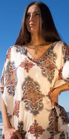 Woman wearing a patterned silk kaftan dress with a v-neck, standing outdoors in sunlight