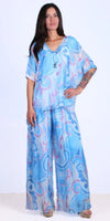 Woman wearing flowy blue and pink patterned silk top and wide-leg pants set