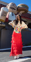 Woman in a colorful patterned sweater and tiered red maxi skirt outdoors, standing by a burger and beer statue.