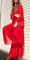 Woman wearing a flowing red sheer blouse and wide-leg pants with sequin details