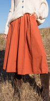 Woman in cream knit sweater and rust orange midi skirt standing outdoors in tall boots